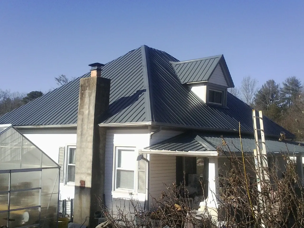Dark blue standing seam metal roof on a white farmhouse with dormer — Slate & Tile Roof Repair by Roofing Brothers in Johnston