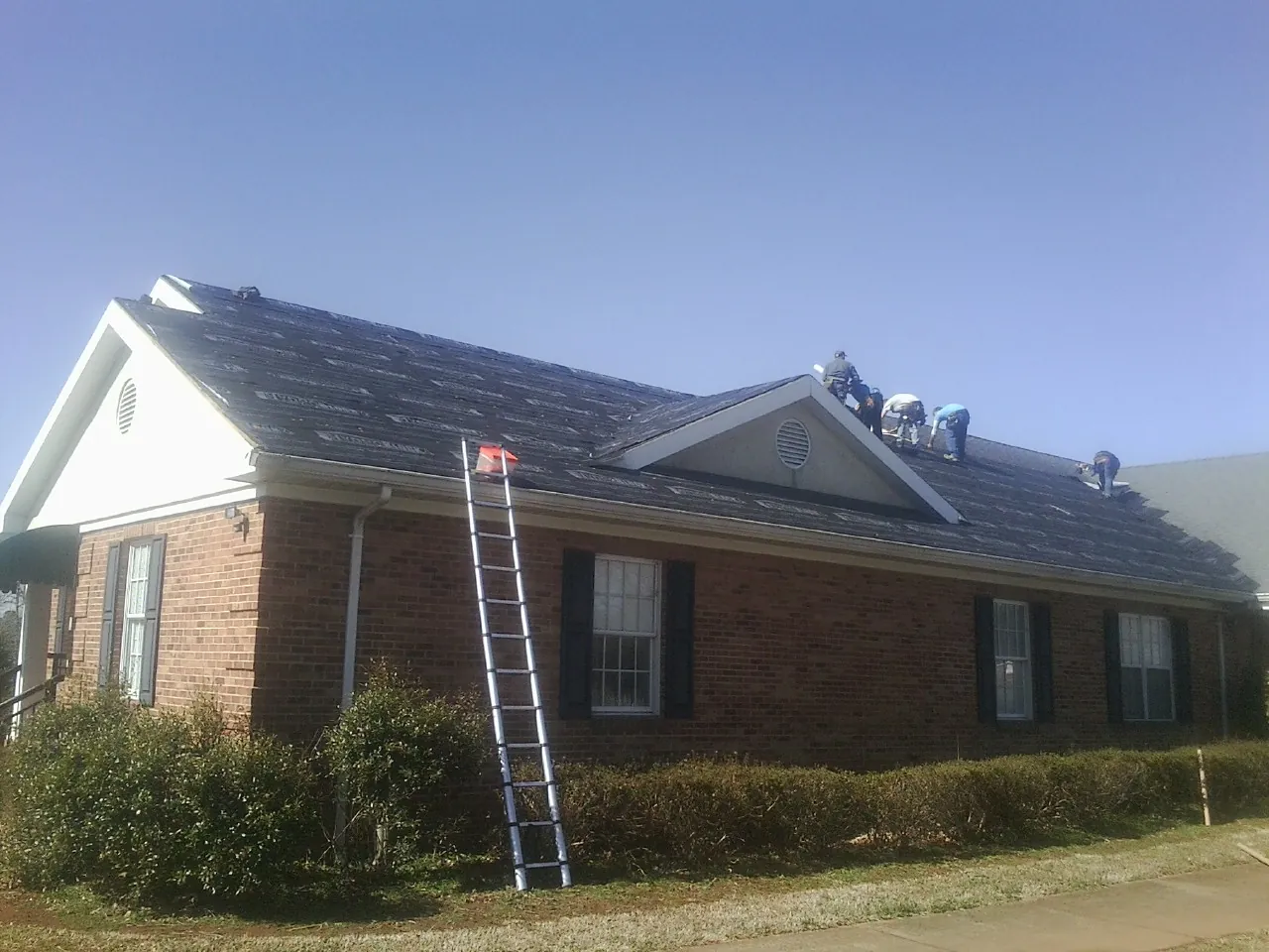 Crew tearing shingles off a brick ranch roof with a ladder set — Metal Roof Repair work by our crew in Johnston