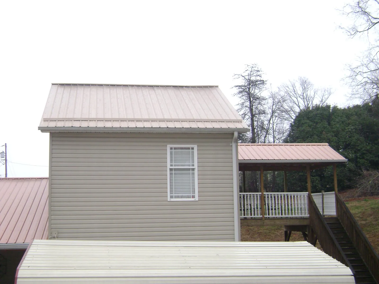 Tan metal roofs on a two story addition and attached porch, from a Roof Replacement job in Johnston